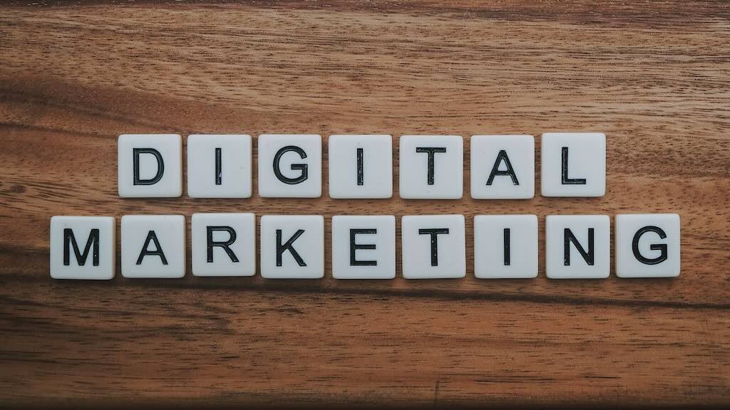 White letter tiles on a wooden surface spelling out the words DIGITAL MARKETING.