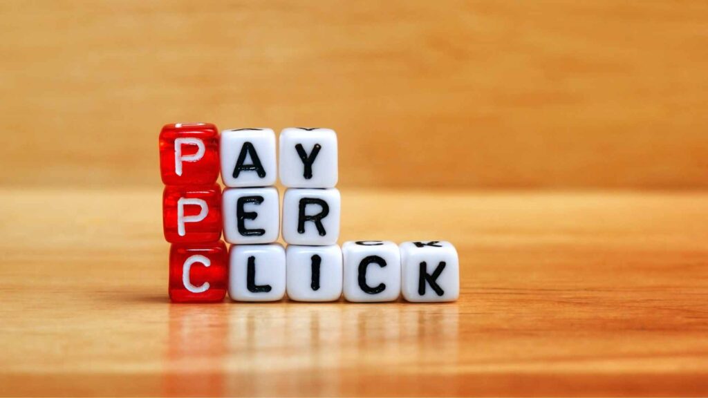 Letter blocks on a wooden table spelling out PAY PER CLICK in red and white.