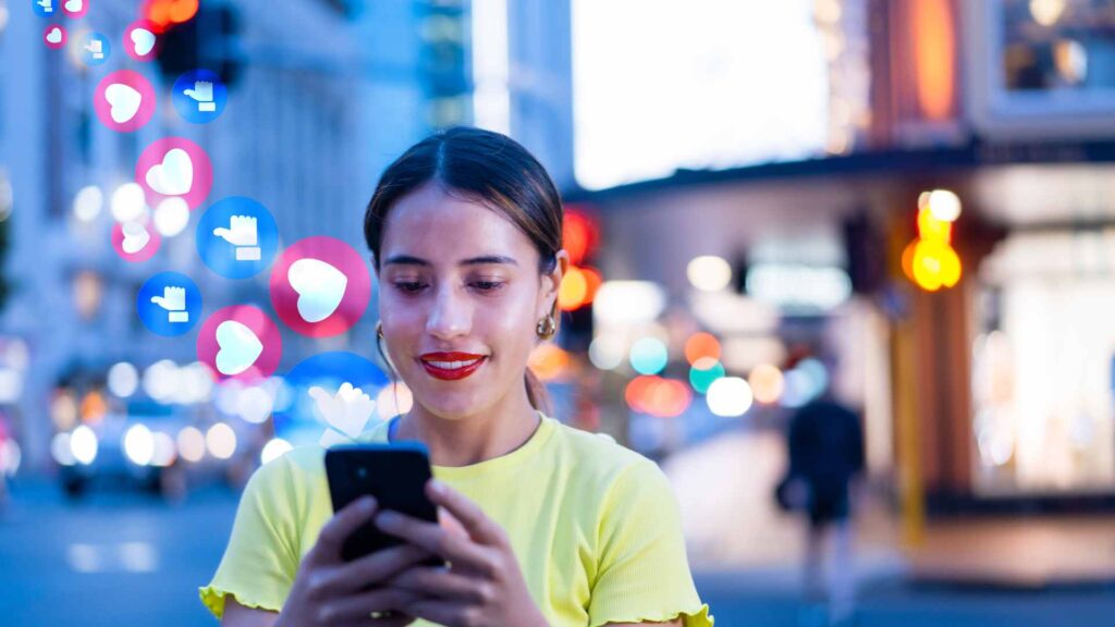 A woman at night smiles while looking at her smartphone as 'like' and 'heart' notification icons float around her.